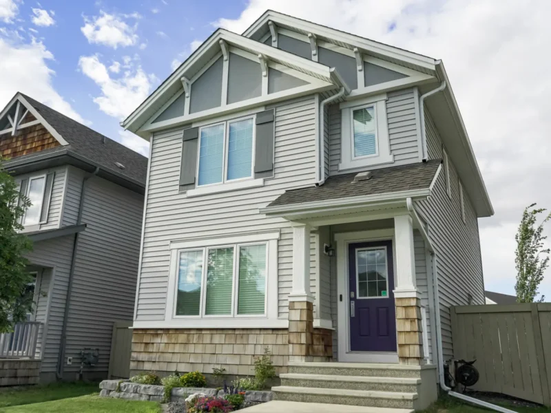 Two storey home finished with light grey siding and stone accents