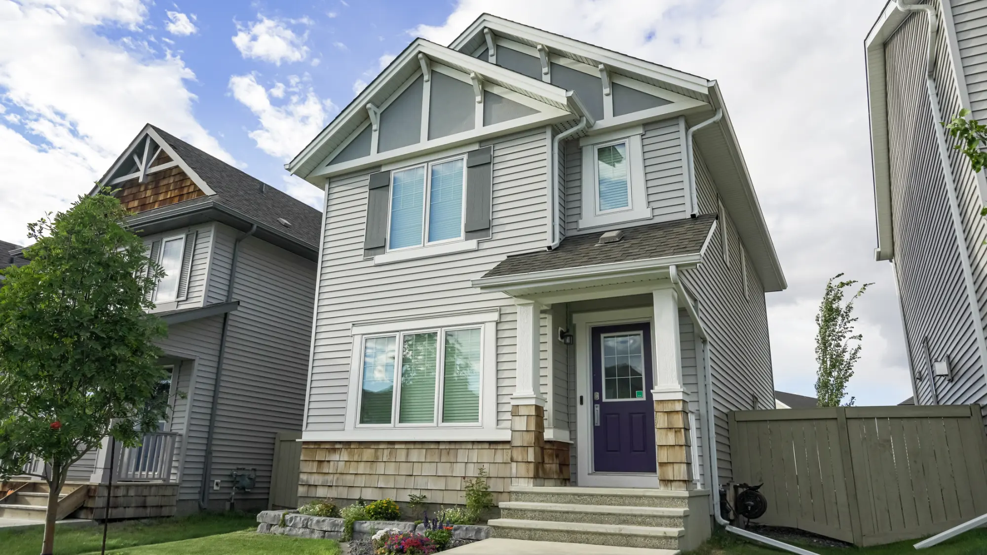 Two storey home finished with light grey siding and stone accents