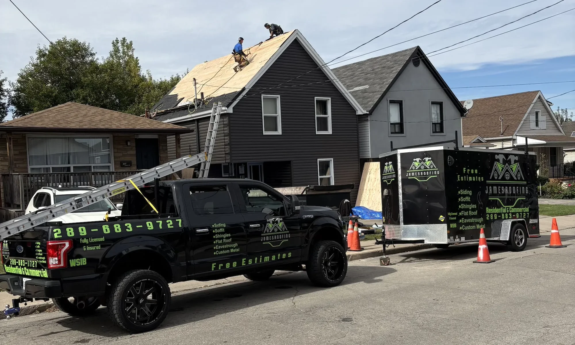 James Roofing crew in fall protection harnesses installing new roof sheathing, with the James Roofing truck and trailer parked out front