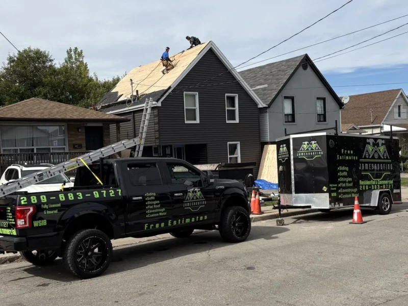 James Roofing crew in fall protection harnesses installing new roof sheathing, with the James Roofing truck and trailer parked out front