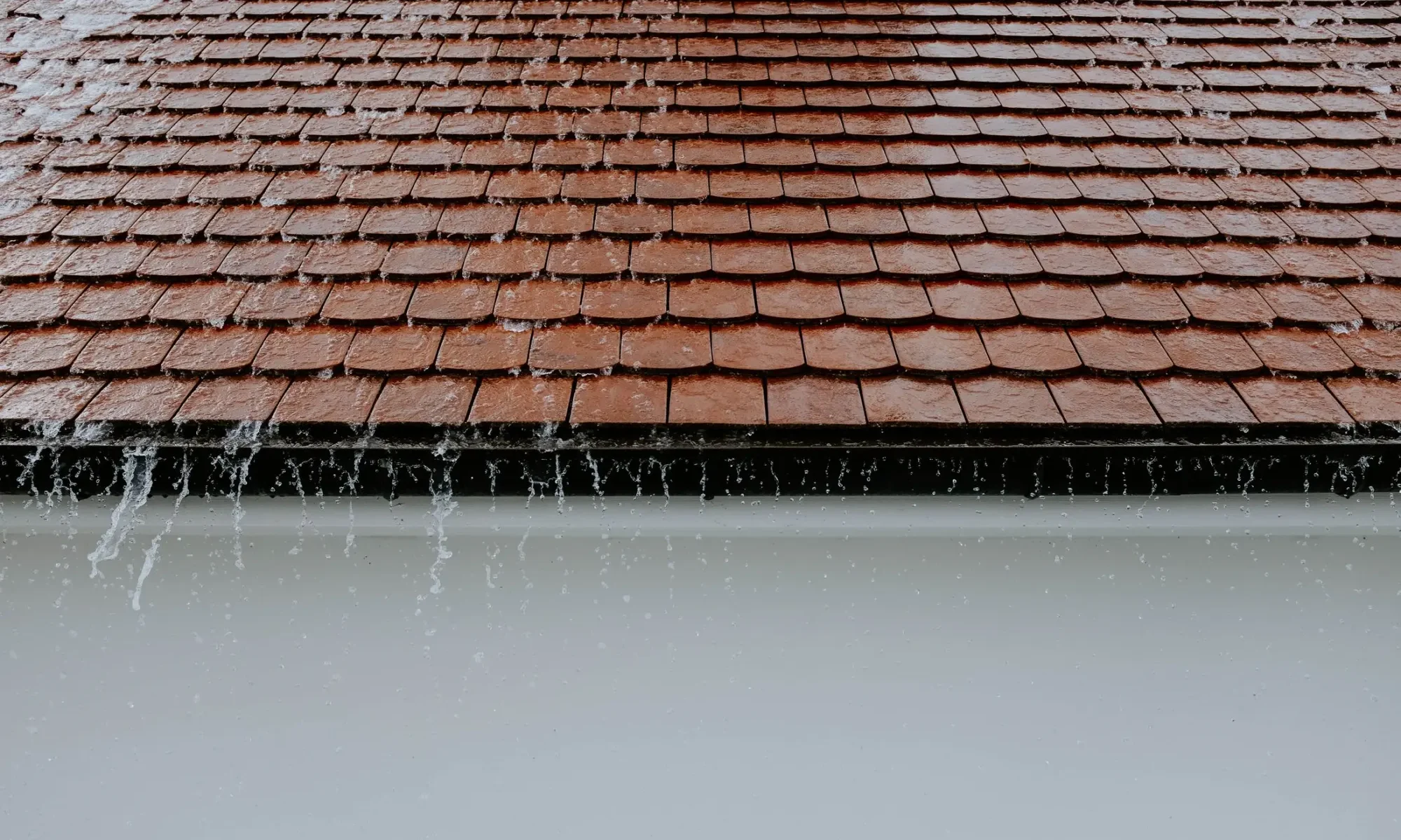 Rain flowing off roof shingles into a gutter