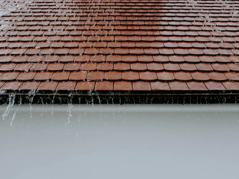 Rain flowing off roof shingles into a gutter