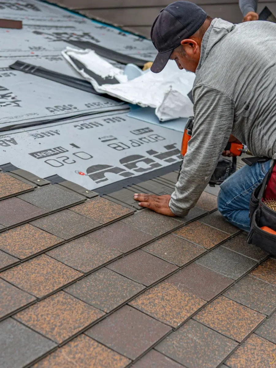 Roofer kneeling on a roof installing architectural asphalt shingles