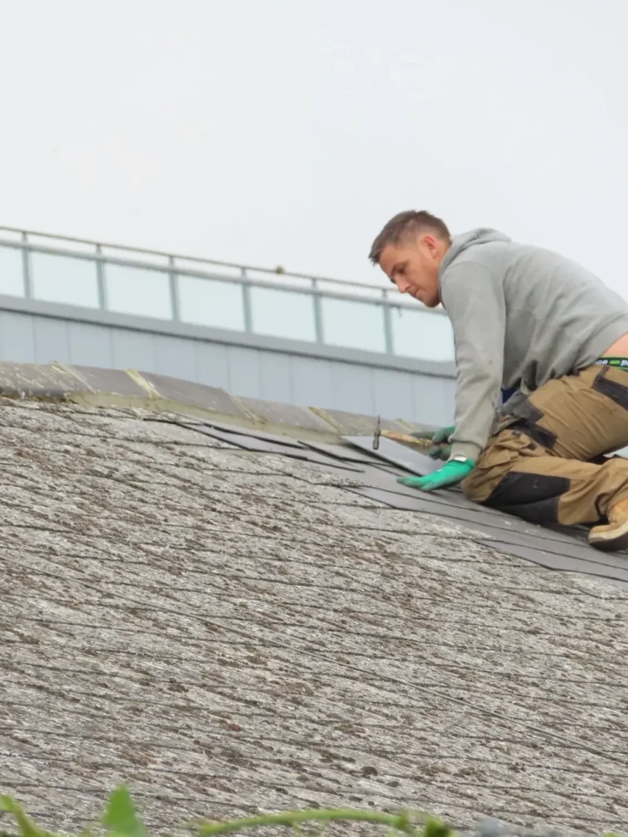 Roofer kneeling on a shingle roof making a repair