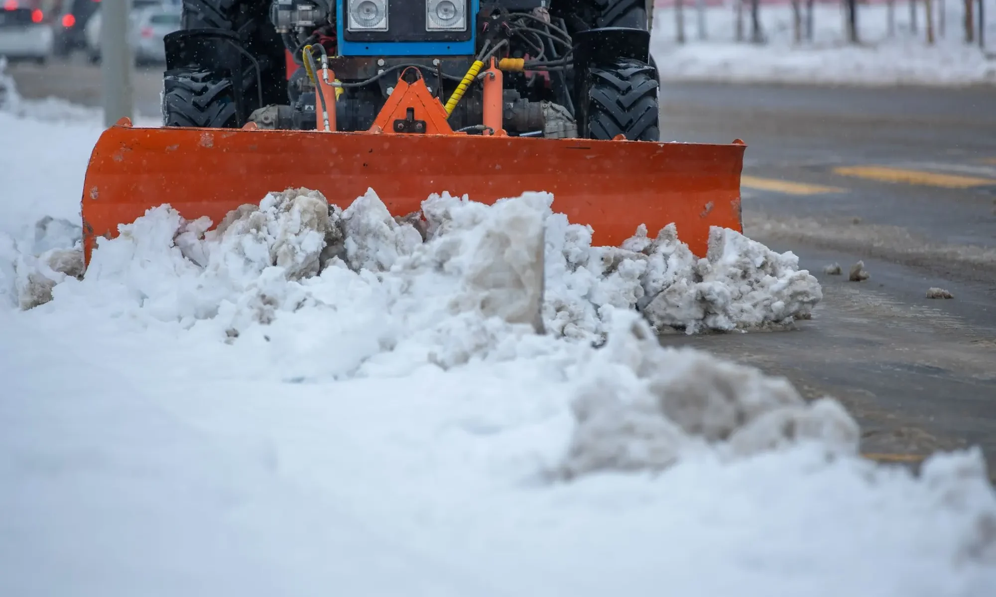 Snow plow blade clearing deep snow from a paved lot