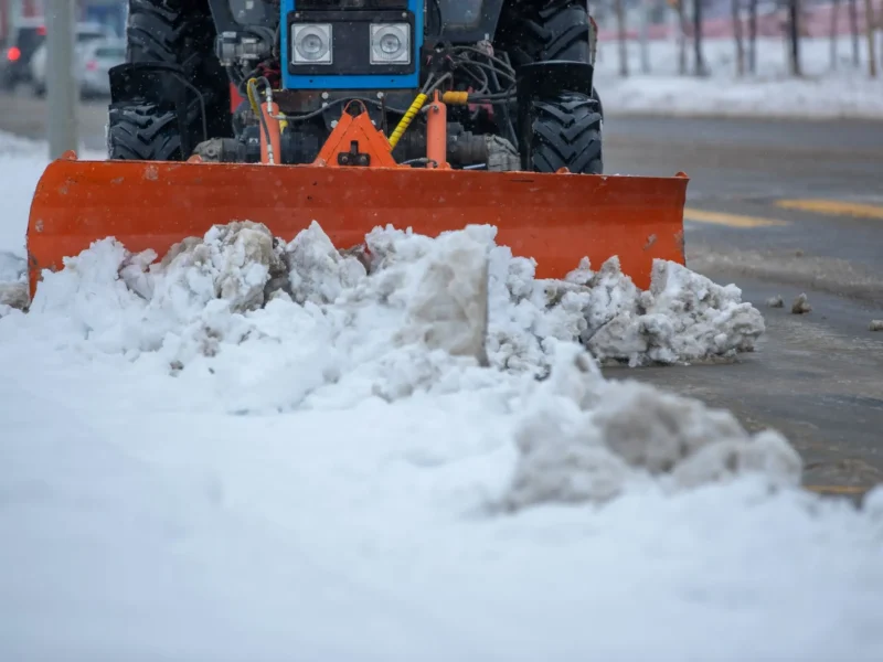 Snow plow blade clearing deep snow from a paved lot